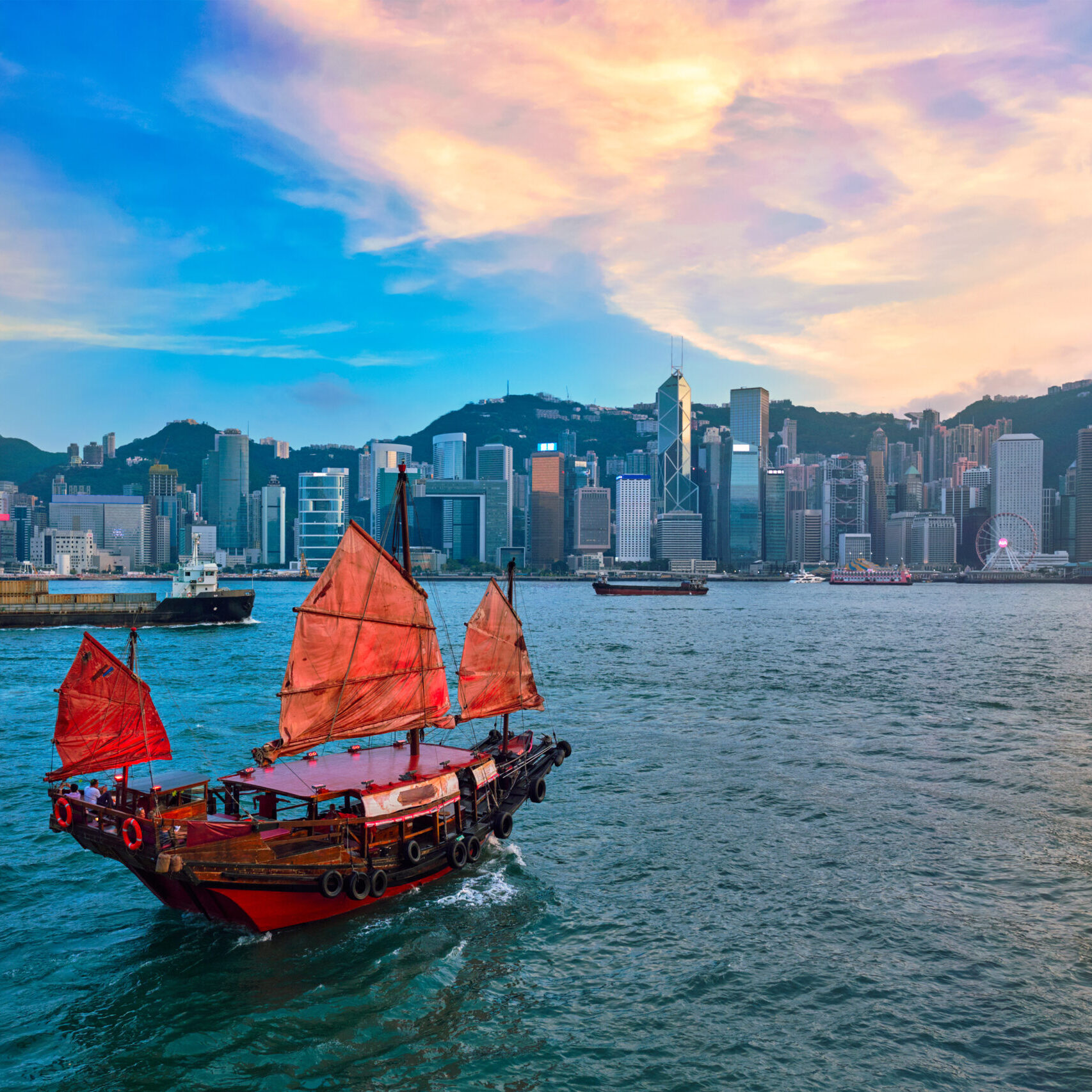 Hong Kong skyline cityscape downtown skyscrapers over Victoria Harbour in the evening with junk tourist ferry boat on sunset with dramatic sky. Hong Kong, China